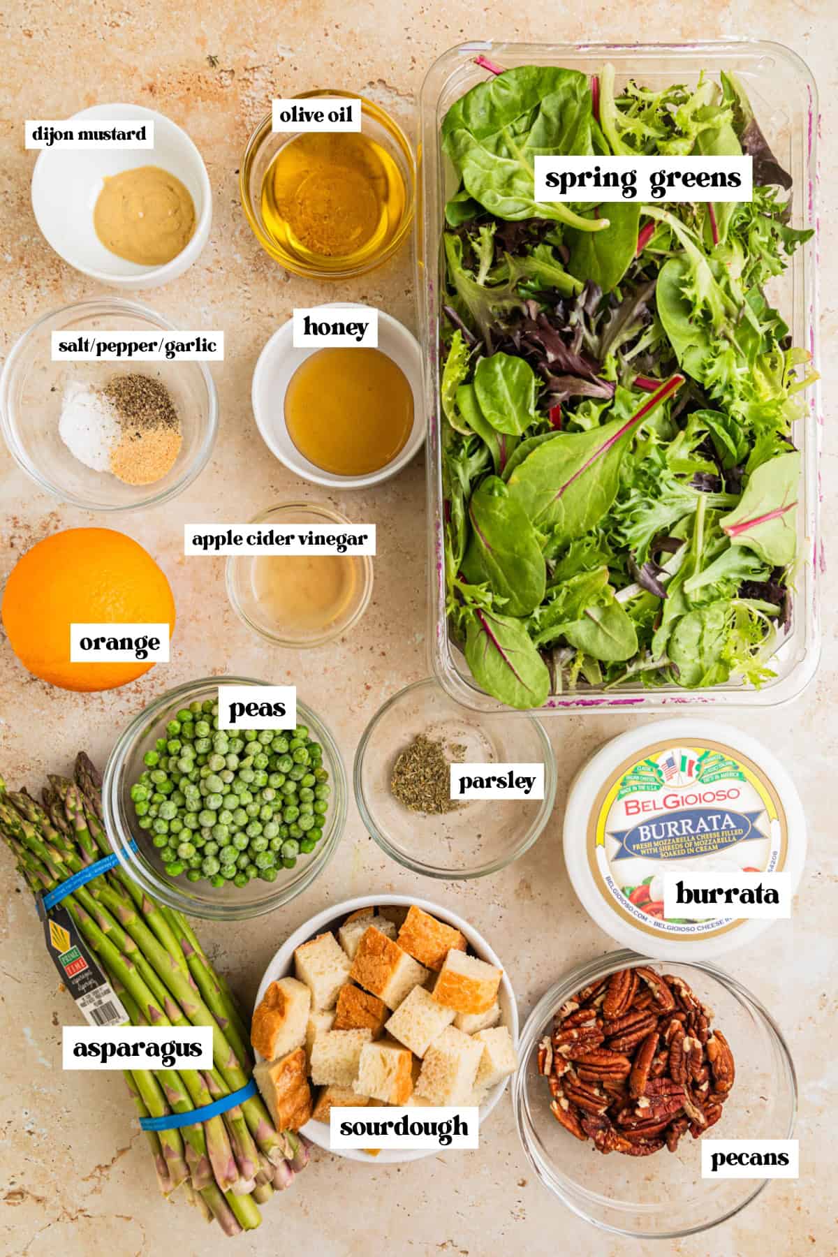Mixed greens, bread cubes, burrata cheese, asparagus and other salad ingredients arranged on surface.