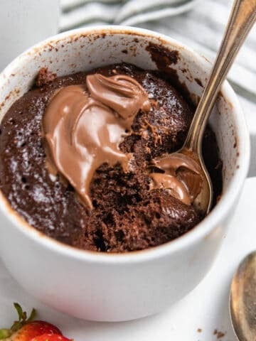 Flourless Nutella mug cake in mug with spoon and extra dollop of Nutella.