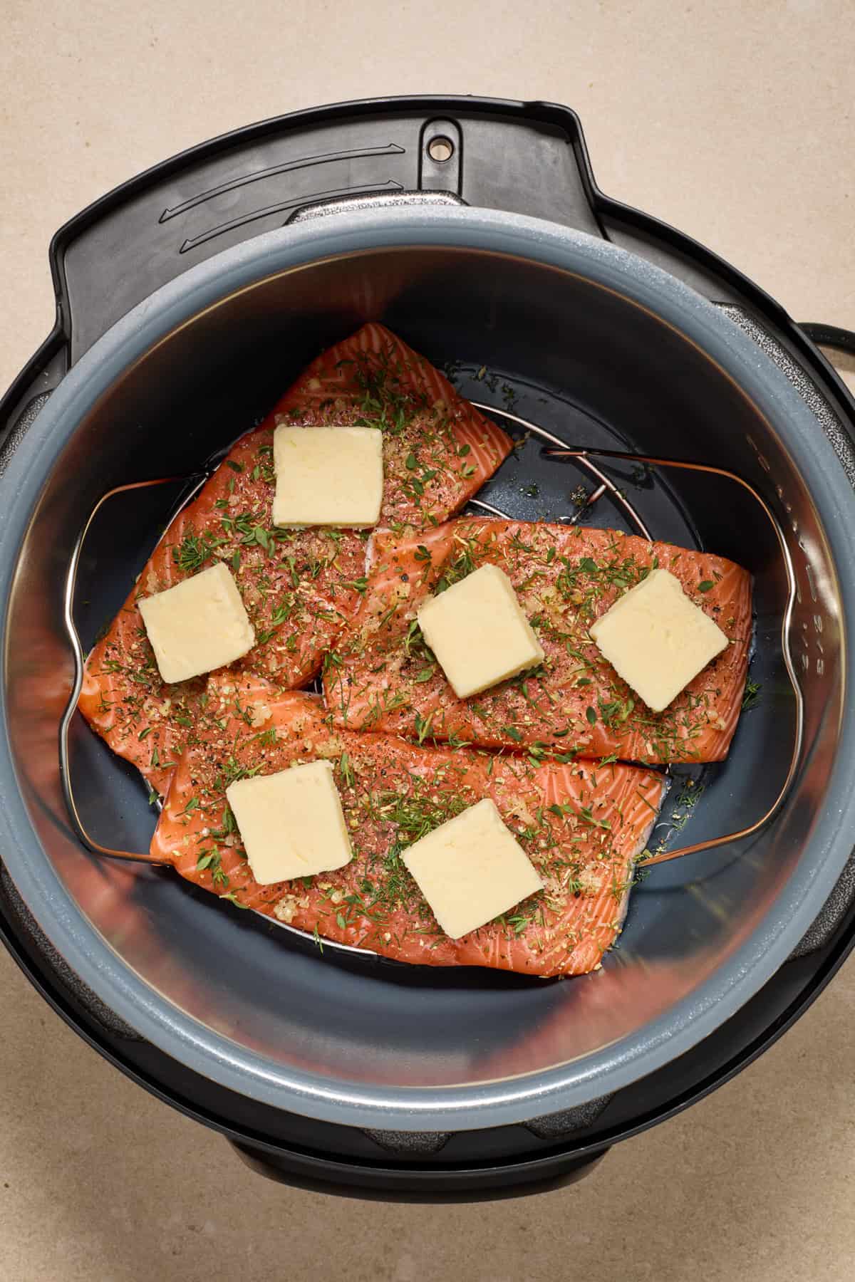 Pressure cooker pot with salmon that has fresh herbs and butter on top.