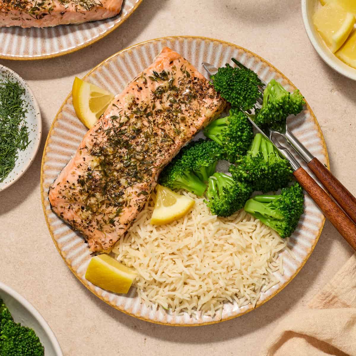 Plate with herbed salmon served with broccoli and rice with lemon wedges.