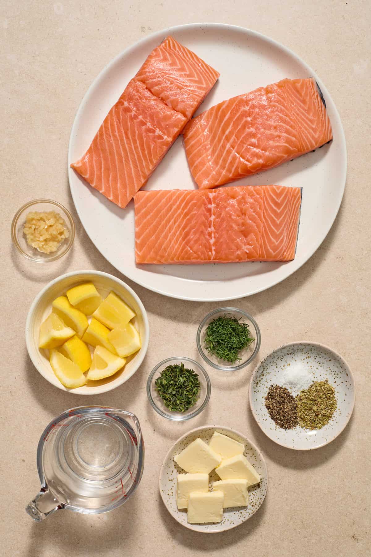 Salmon, herbs, butter, lemons and other ingredients on surface.