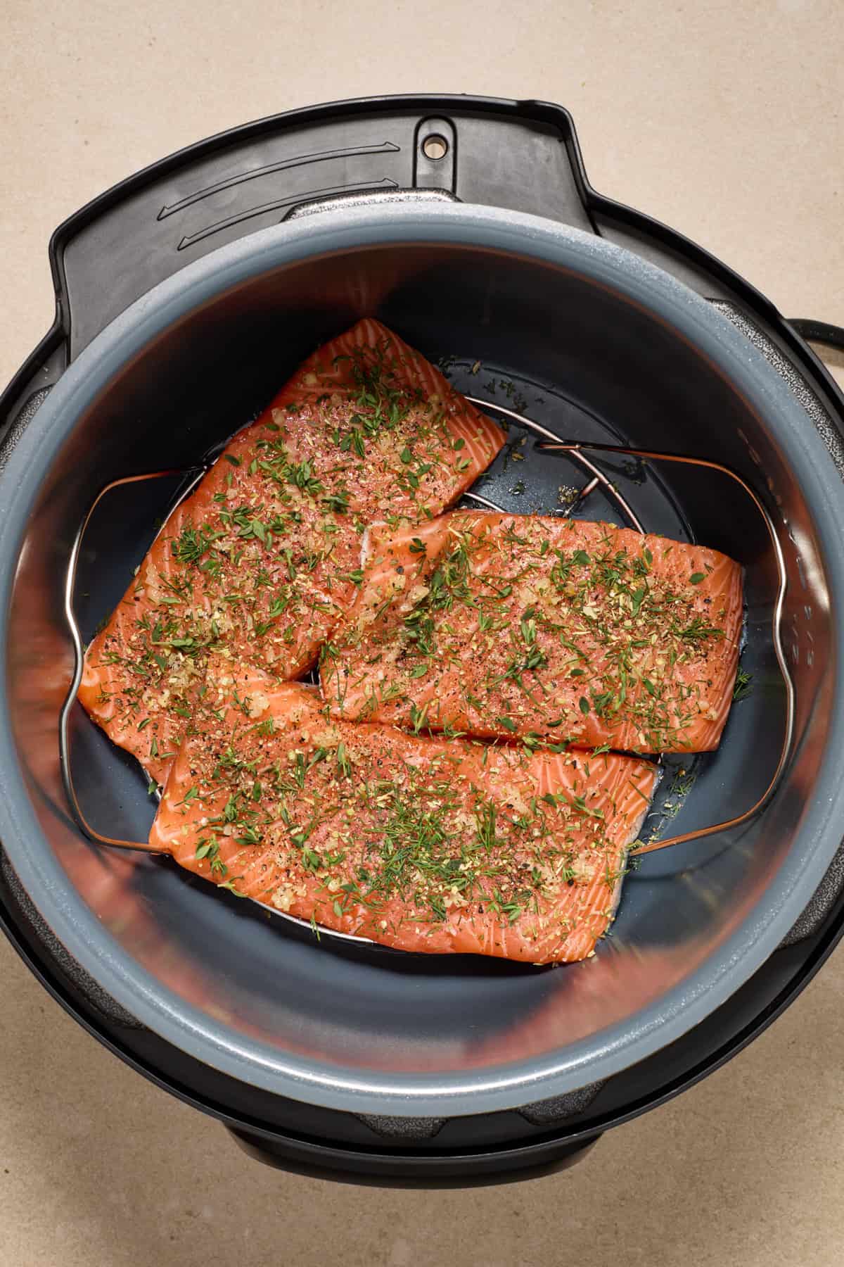 Seasoned salmon filets in instant pot with fresh herbs over top.