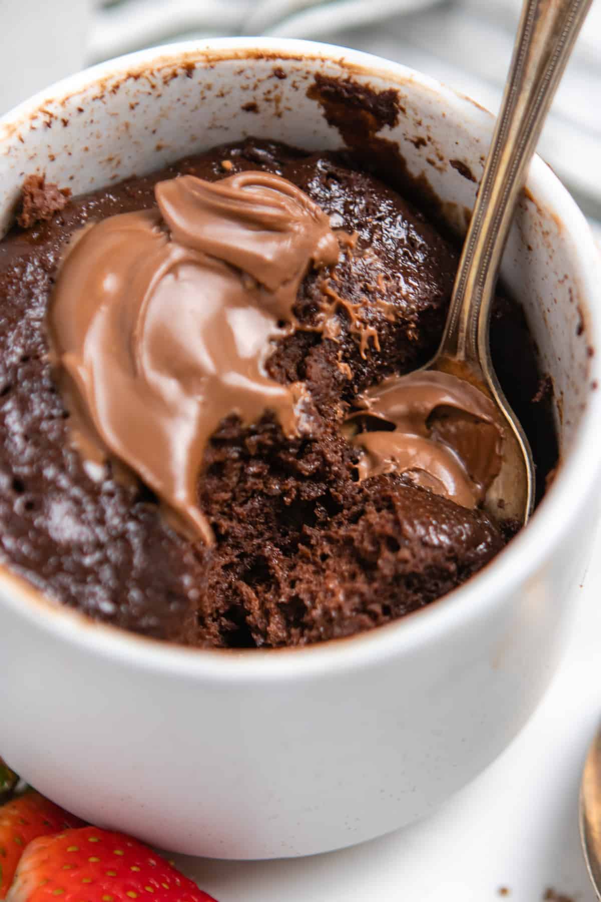 Flourless nutella mug cake in mug with dollop of nutella on top and spoon.