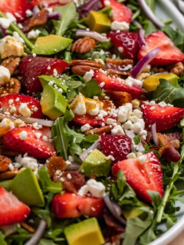 Strawberry arugula goat cheese salad on white serving plate topped with balsamic dressing.