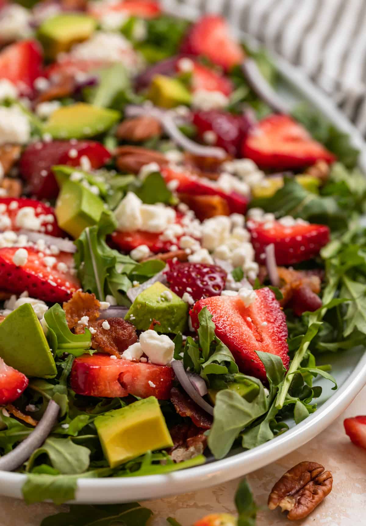 Strawberry goat cheese salad on white plate with avocado, arugula, bacon and pecans.