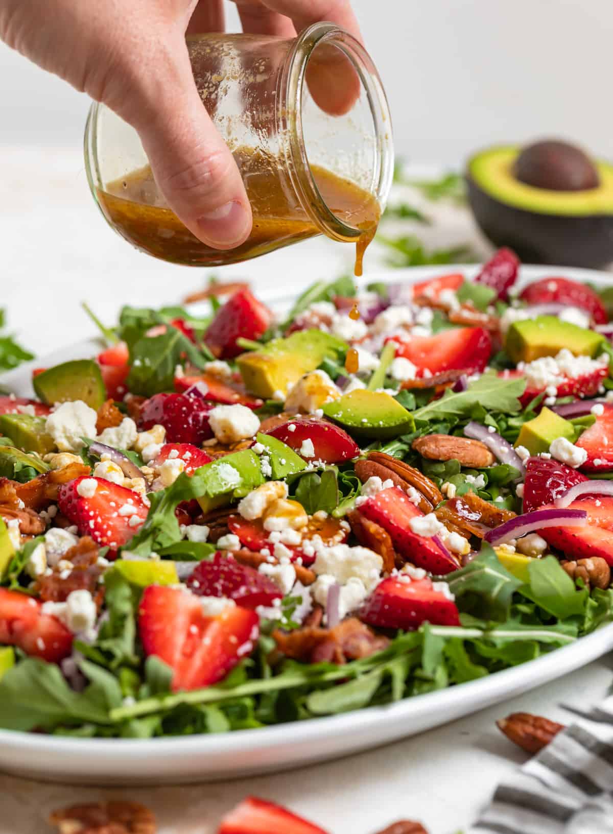 Balsamic dressing being poured over strawberry goat cheese salad on white plate.