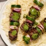 Steak kabobs arranged on a plate over rice and topped with cilantro chimichurri.