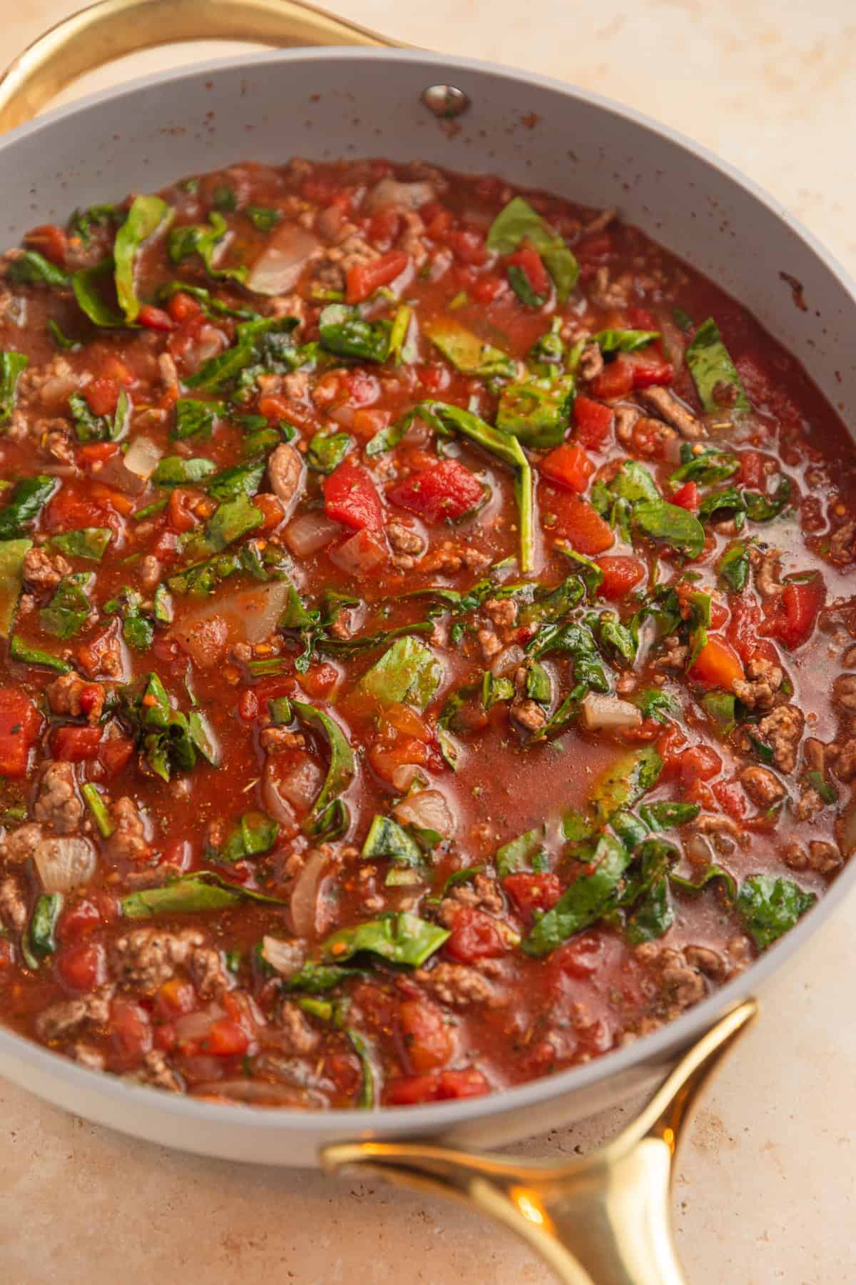 Beef, broth, tomatoes and other ingredients simmering in skillet.