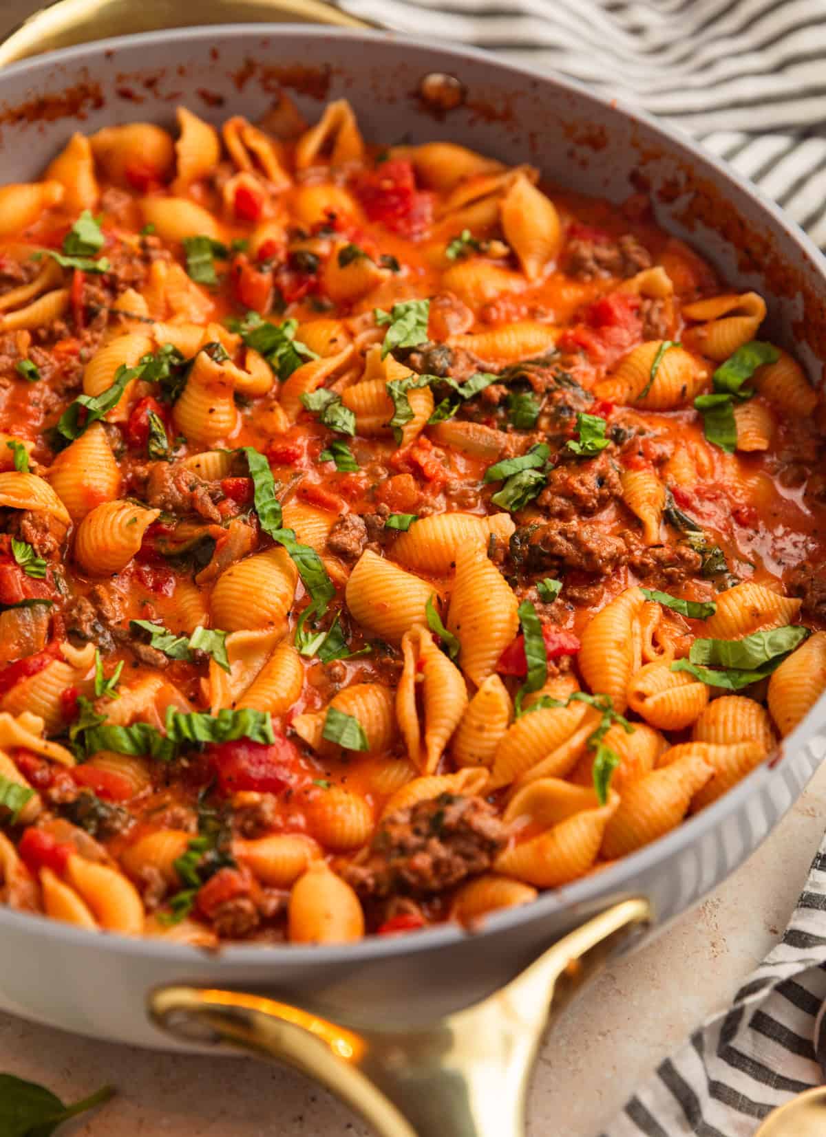 Beef and shells in pan with basil over top.