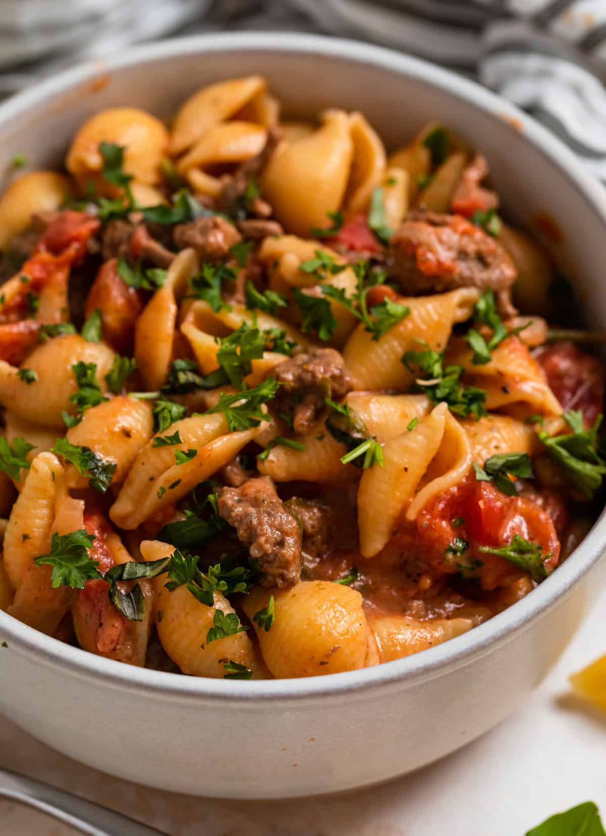 Ground beef and shells pasta in bowl with fresh parsley and basil on top.