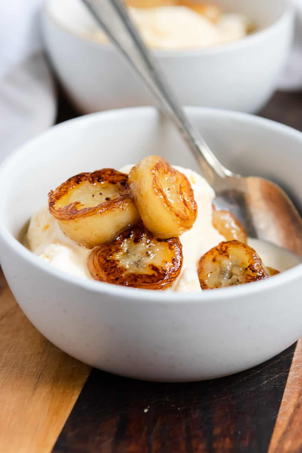 Fried bananas in bowl with vanilla ice cream and spoon.