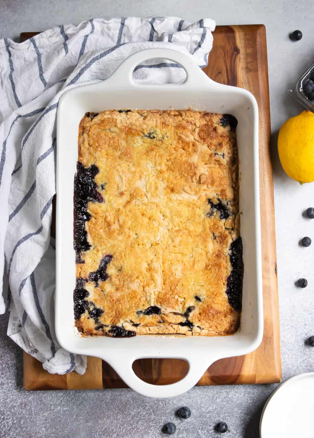 Overhead view of blueberry dump cake on wood board with napkin and lemons.