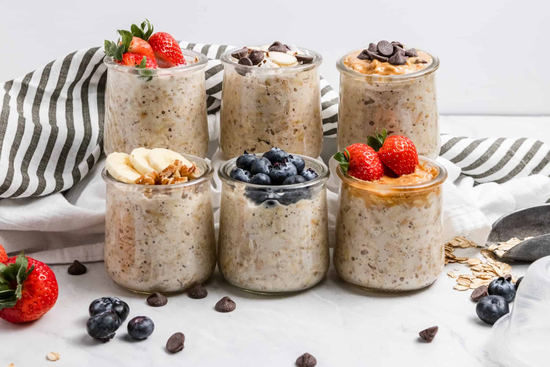 6 jars of overnight oats with ingredients surrounding.