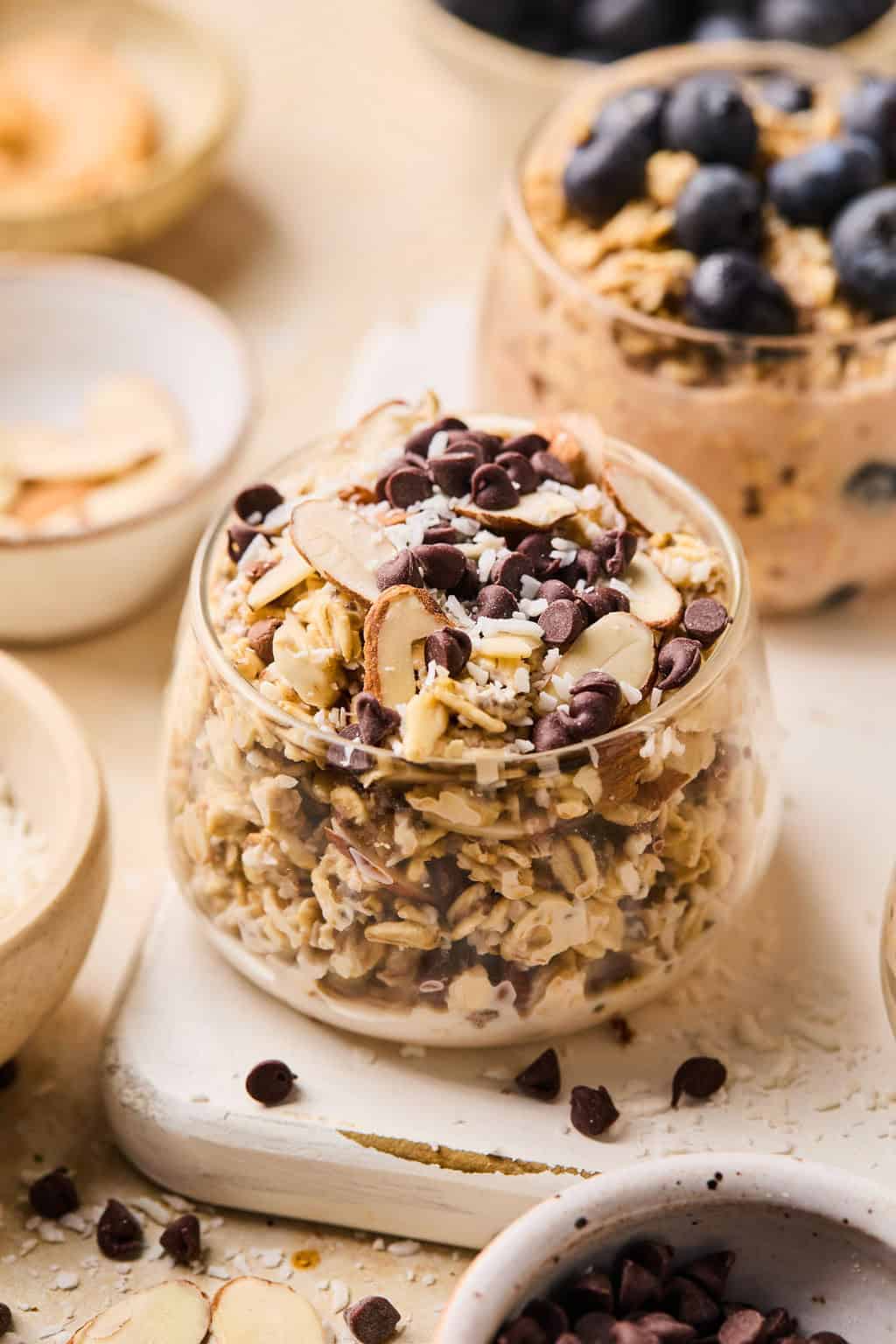 Almond, coconut and chocolate chip oats in glass with other dishes surrounding.