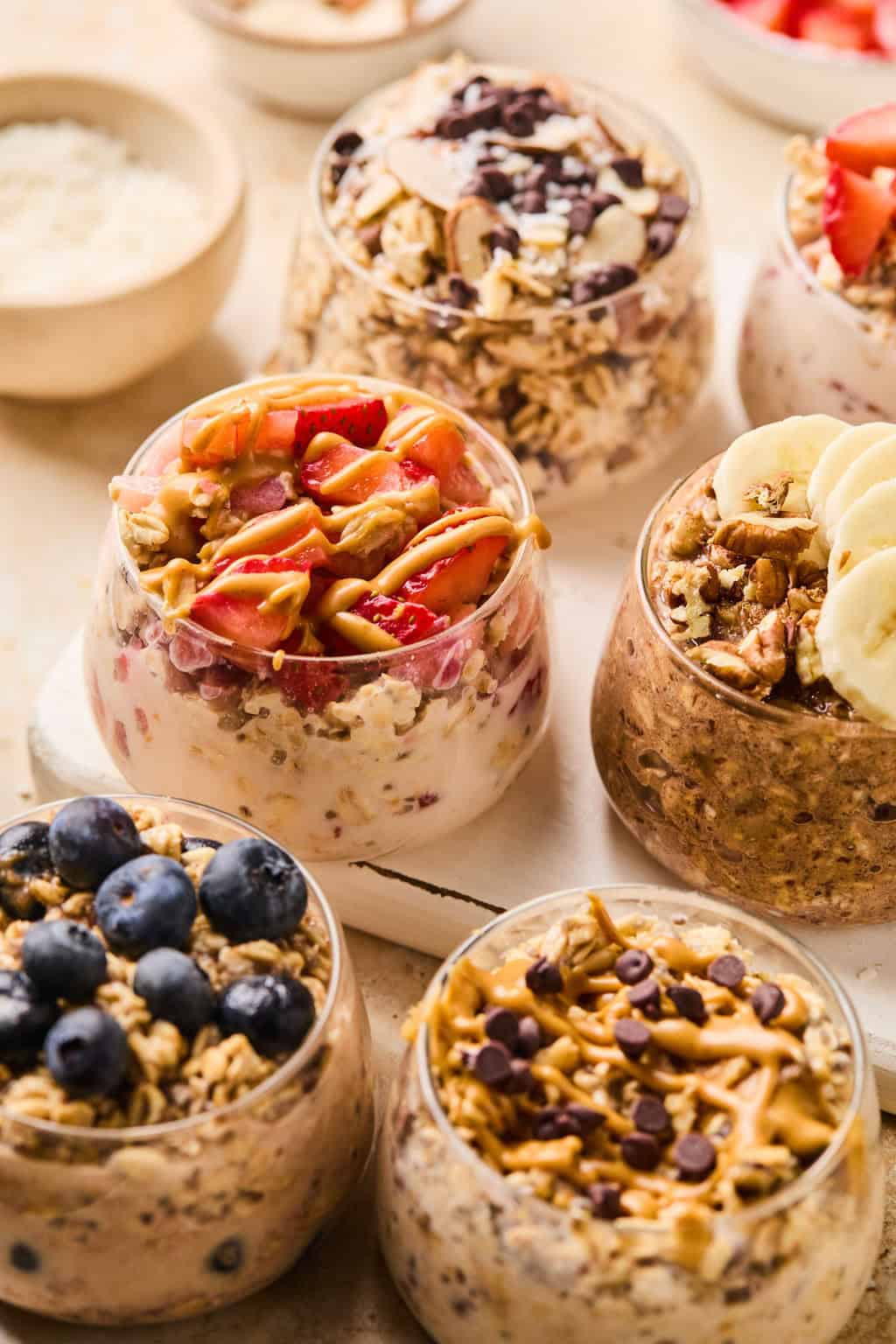 Glasses with overnight oats recipes prepared and topped with different garnishes.