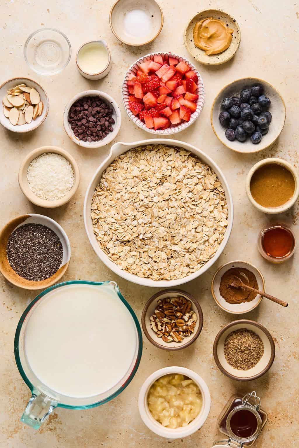 Rolled oats, milk, maple syrup, chia seeds, berries and other ingredients arranged on a surface.