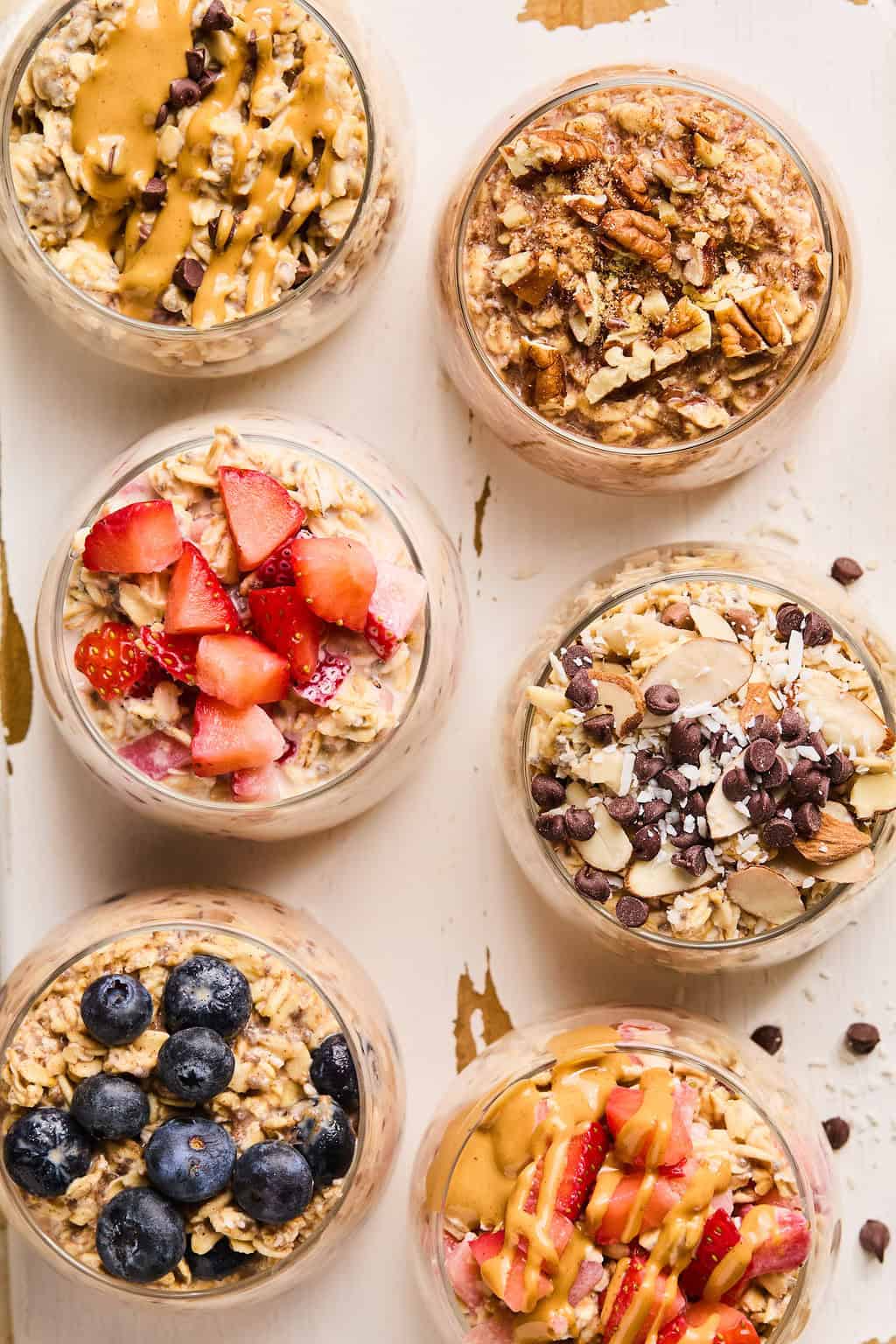 Overhead view of six easy overnight oats recipes prepared in glass dishes including peanut butter and jelly, blueberry muffin, peanut butter chocolate and more.