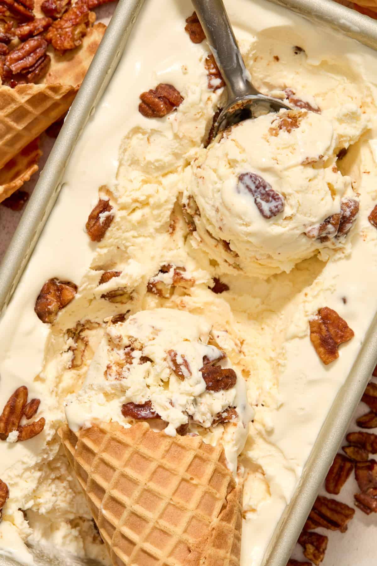 Ice cream scoop with butter pecan homemade ice cream in it and then a waffle cone propped in the container.