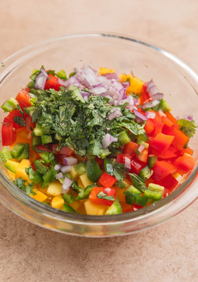Diced mango, red bell pepper, onion and other salsa ingredients in mixing bowl.