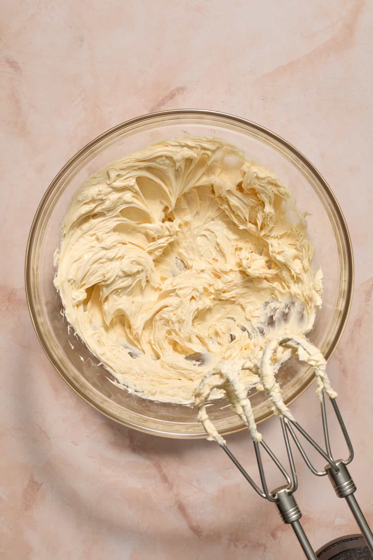 Butter creamed in glass bowl with mixer propped by the bowl.