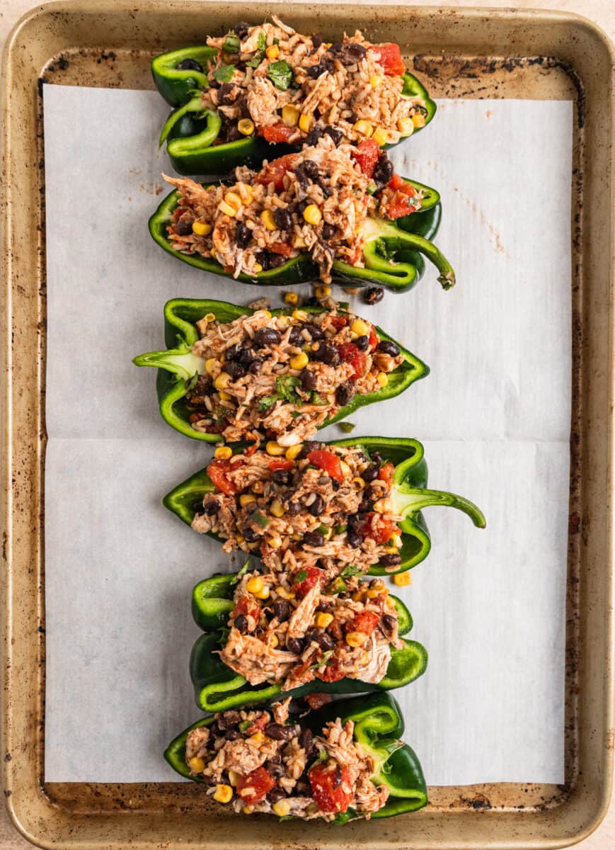 Poblano peppers halved and filled with chicken, rice and bean mixture on baking sheet.