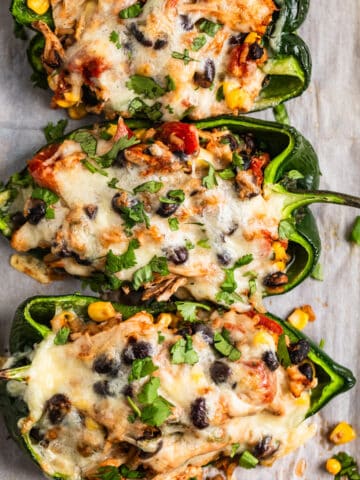 Chicken stuffed poblano peppers on parchment topped with cheese and cilantro.