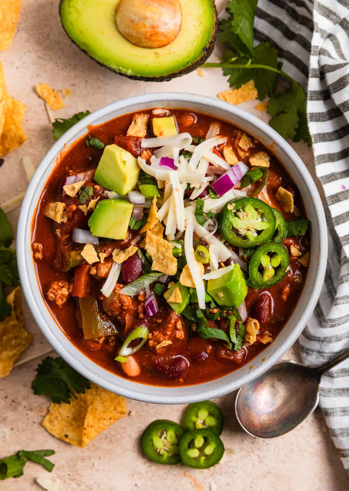 Overhead view of bowl of simple turkey chili topped with cilantro, avocado, corn chips and cheese.