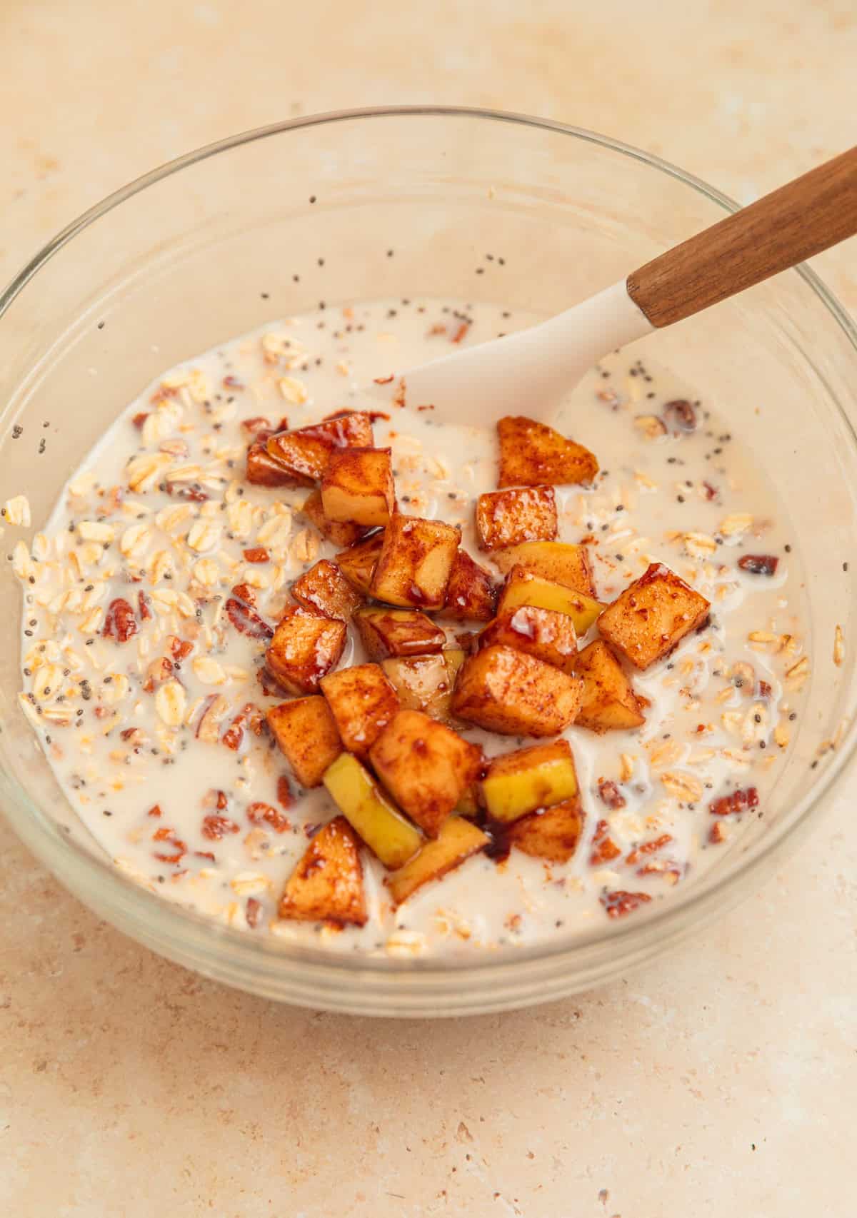Cinnamon apples added to overnight oatmeal mixture in glass bowl.