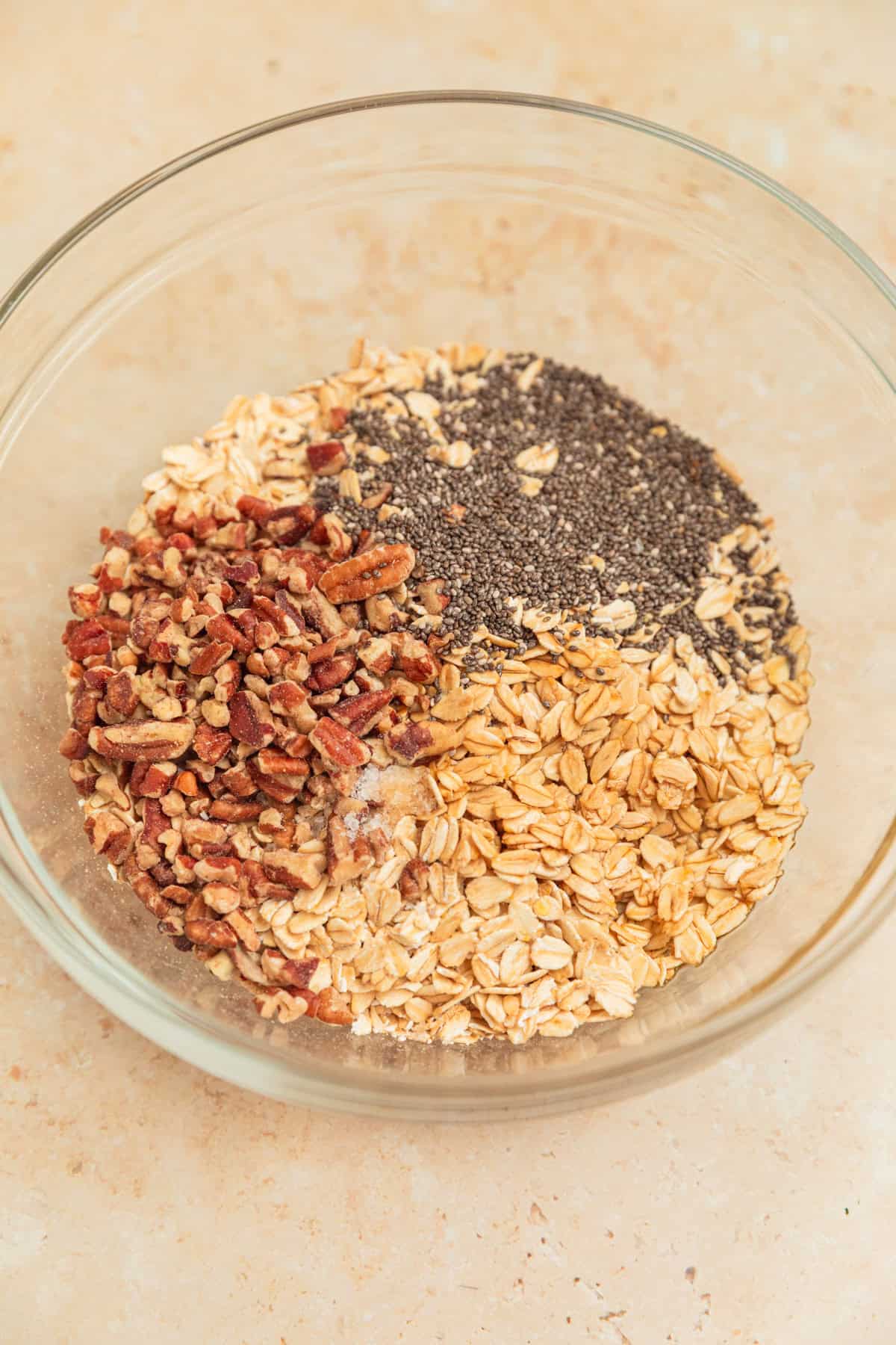 Old fashioned oats, chia seeds, pecans and other ingredients in mixing bowl.