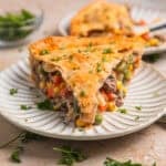 Slice of beef pot pie on plate topped with chopped parsley.