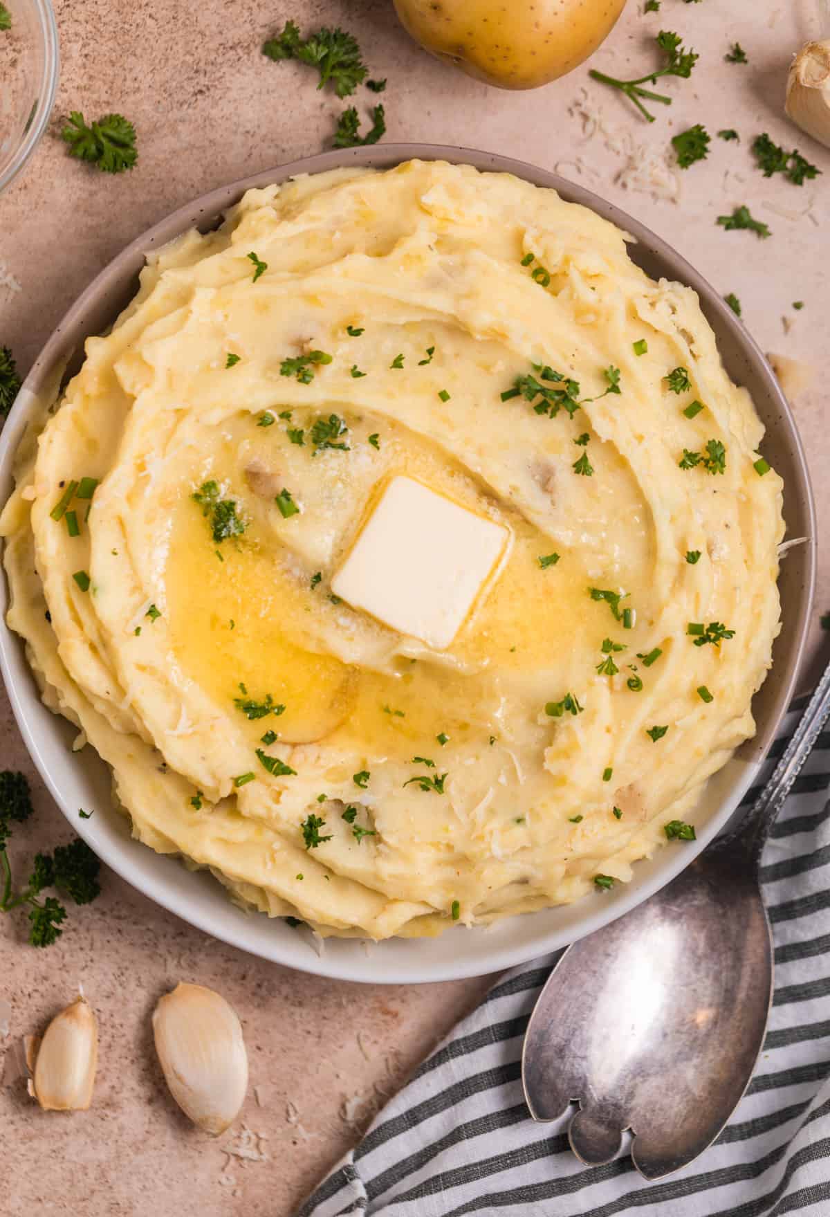 Bowl of Instant pot mashed potatoes topped with butter, chopped parsley and chives on top.