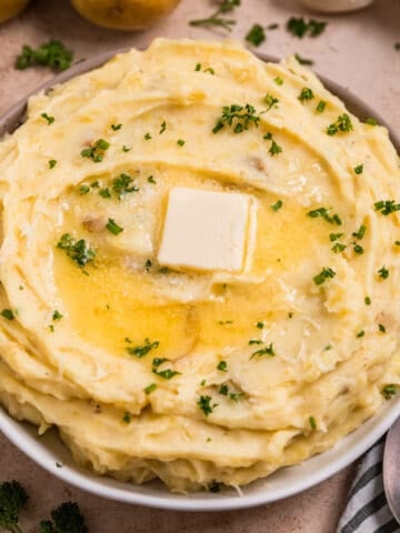 Garlic parmesan mashed potatoes in serving dish with melted butter over top.