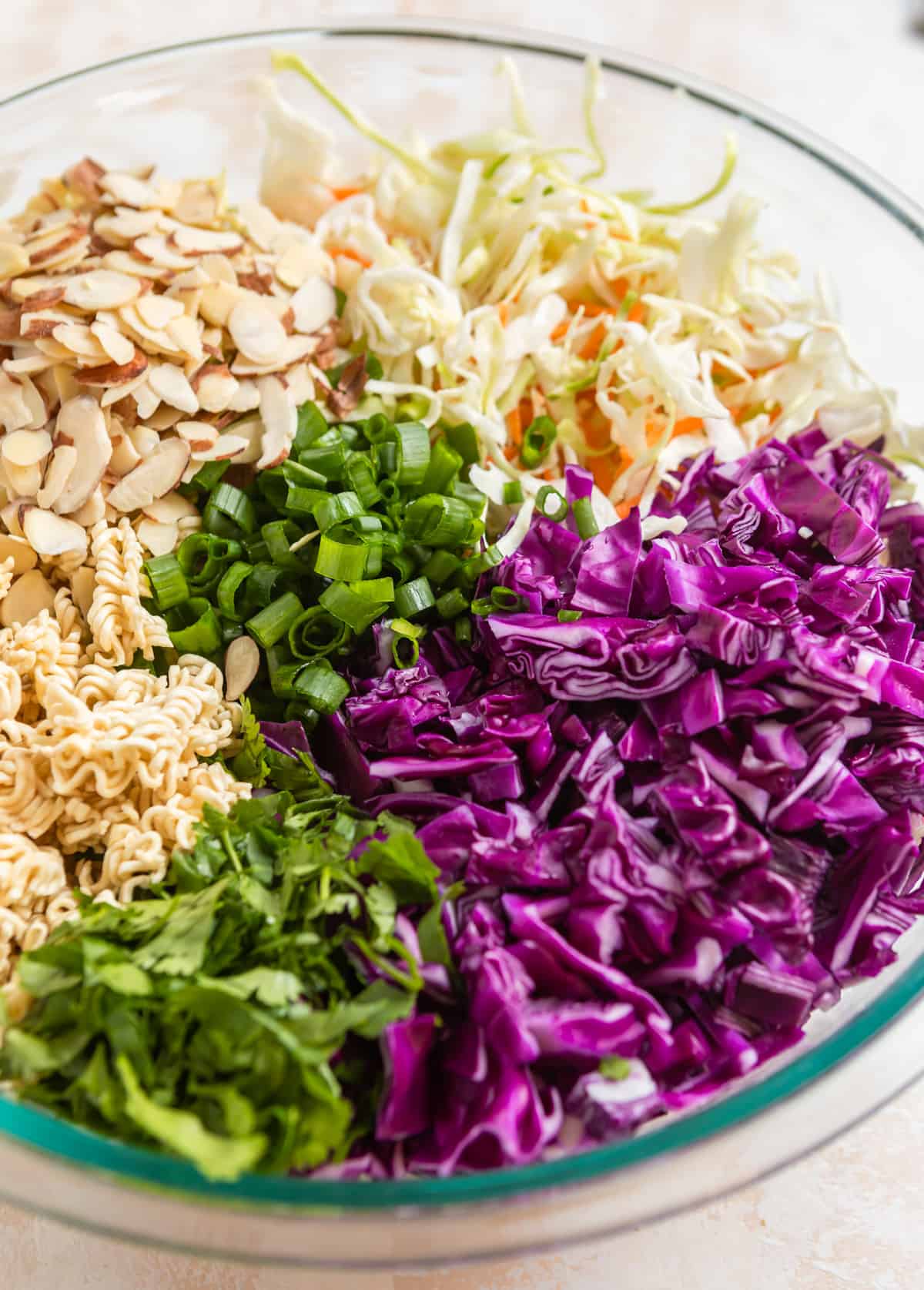 Chopped cabbage, cole slaw mix, almonds, cilantro and cole slaw mix in mixing bowl.