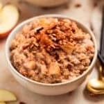 Bowl of apple cinnamon oatmeal topped with chopped pecans.