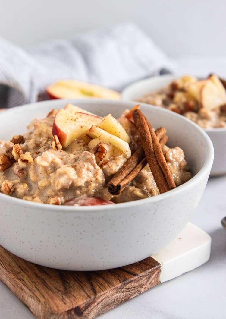 Apple oatmeal in bowl with apples and cinnamon sticks.