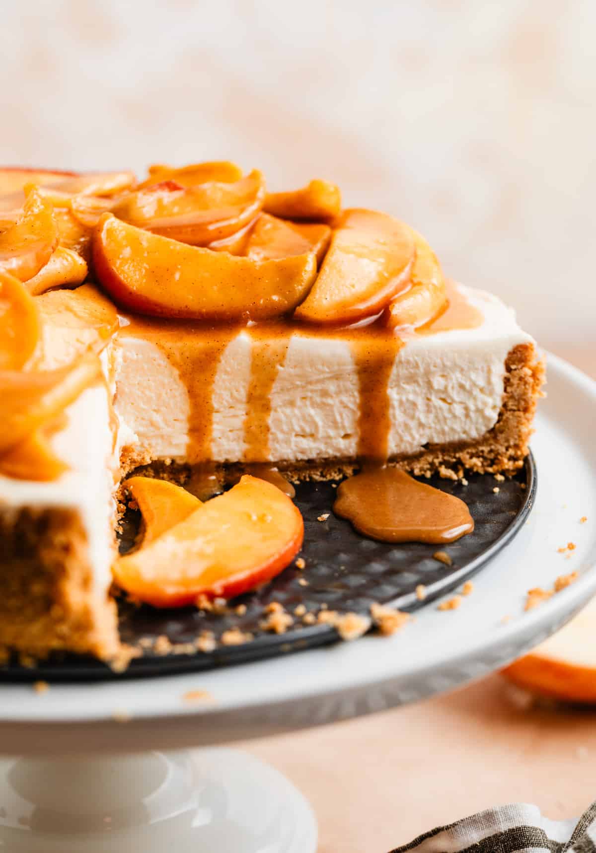 Cheesecake with slice cut out topped with sliced caramel apples and caramel dripping down the sides.
