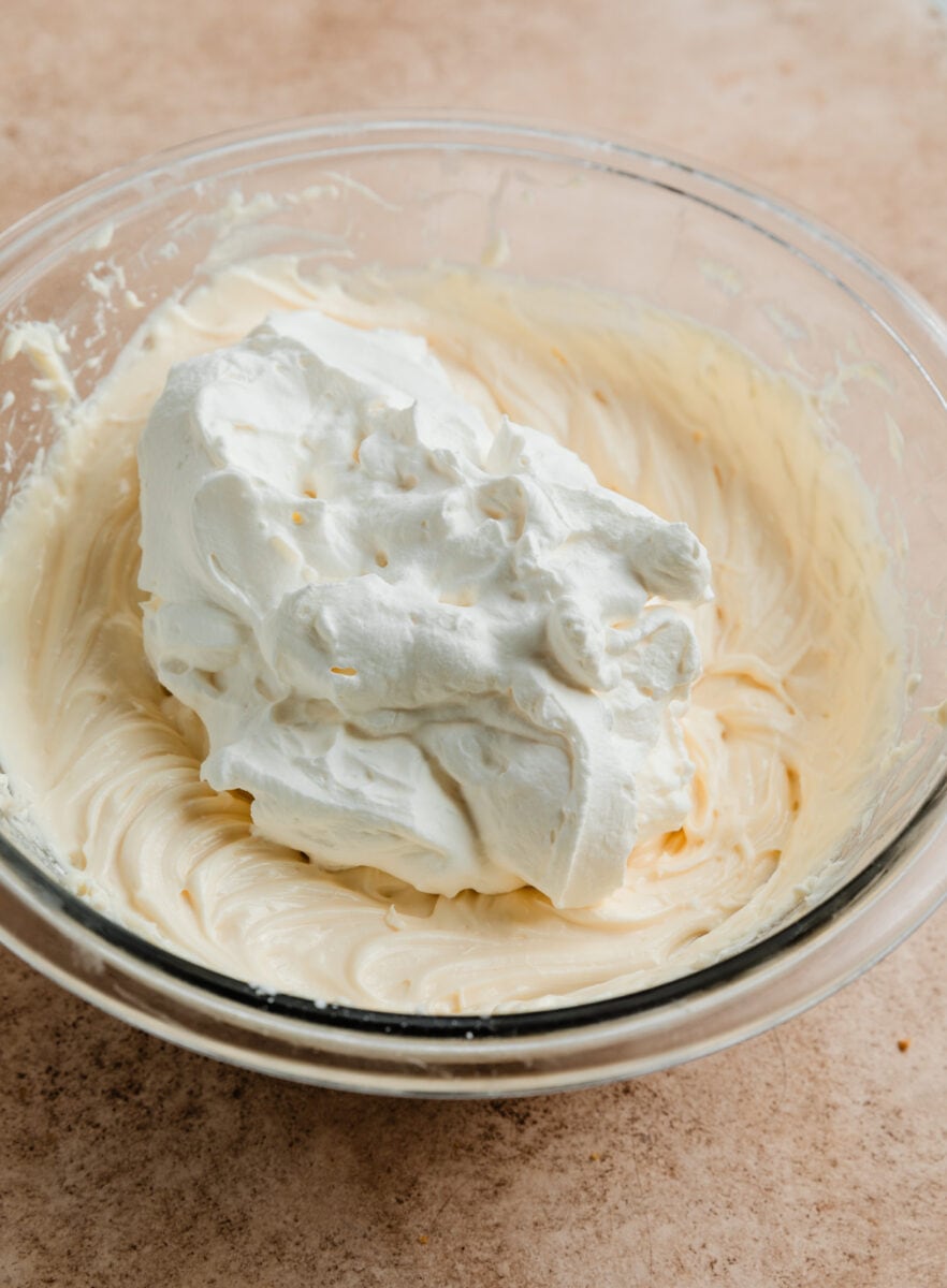 Whipping cream added to cheesecake mixture in glass bowl.