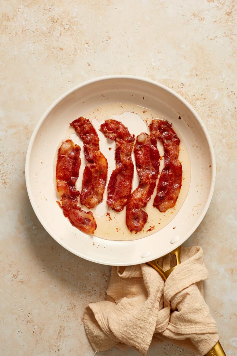 Bacon cooked in skillet with linen around handle.