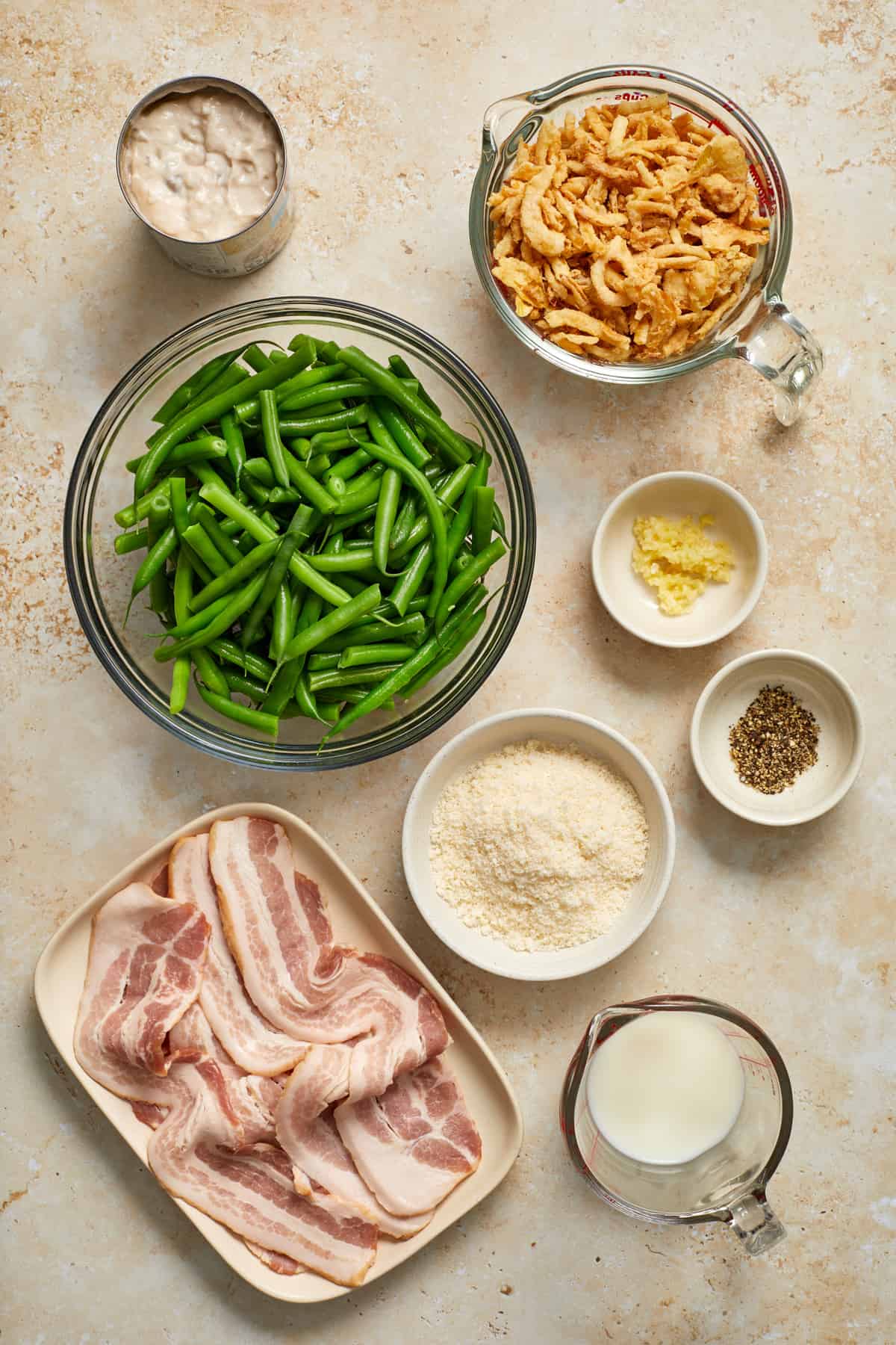 Fried onions, soup, green beans, bacon and other ingredients for recipe arranged on surface.