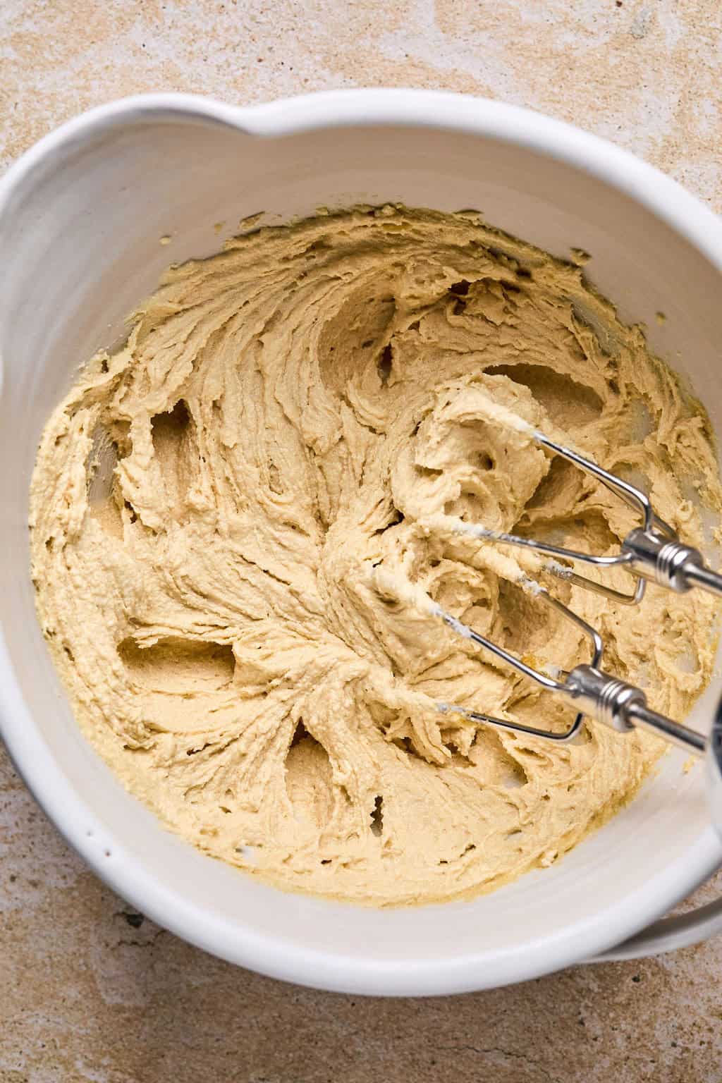 Creamed butter and sugar in mixing bowl with hand mixer propped above.