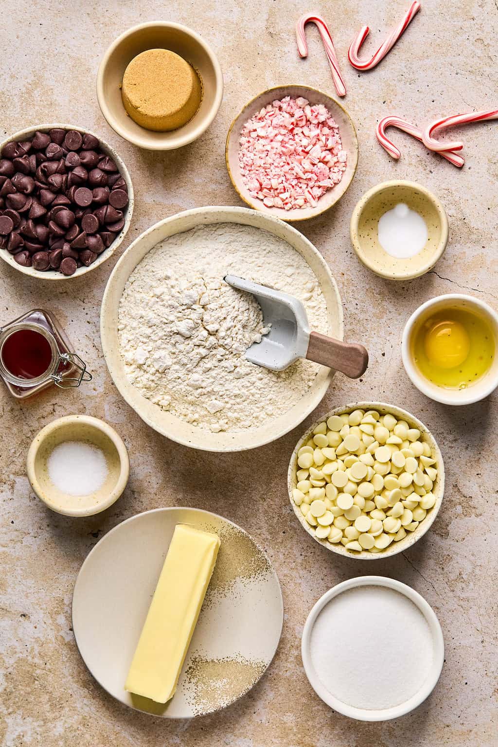 Crushed peppermint candy canes, butter, flour, sugar, egg, chocolate chips and other ingredients arranged on a surface.