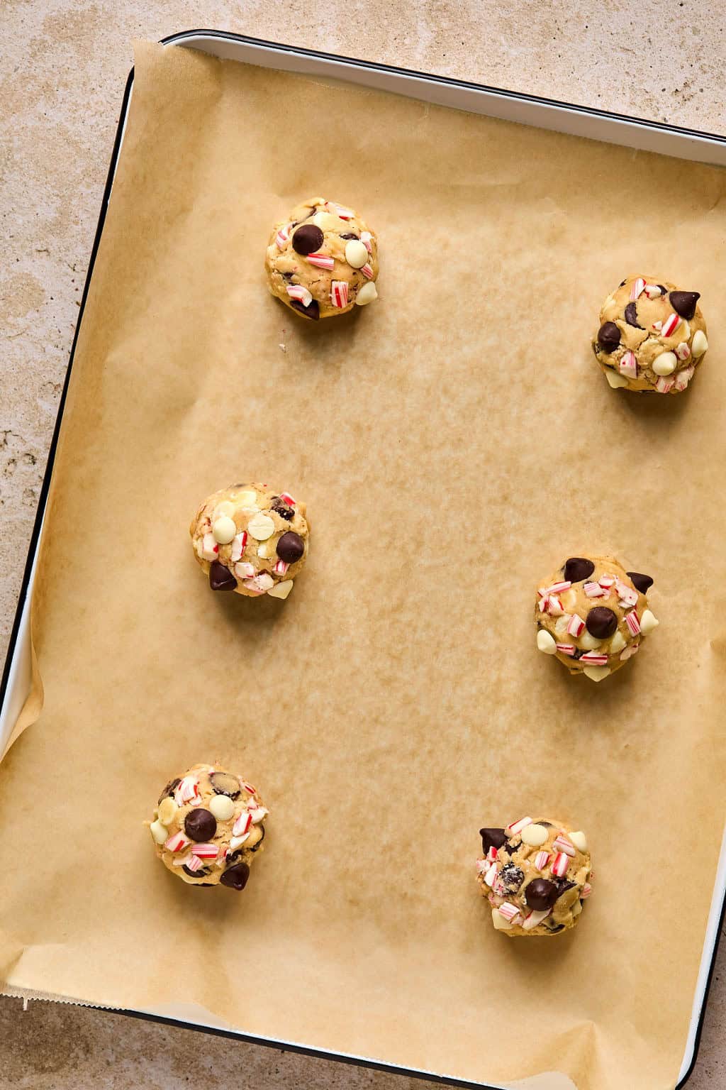 Peppermint candy cane cookie balls on parchment lined baking sheet.