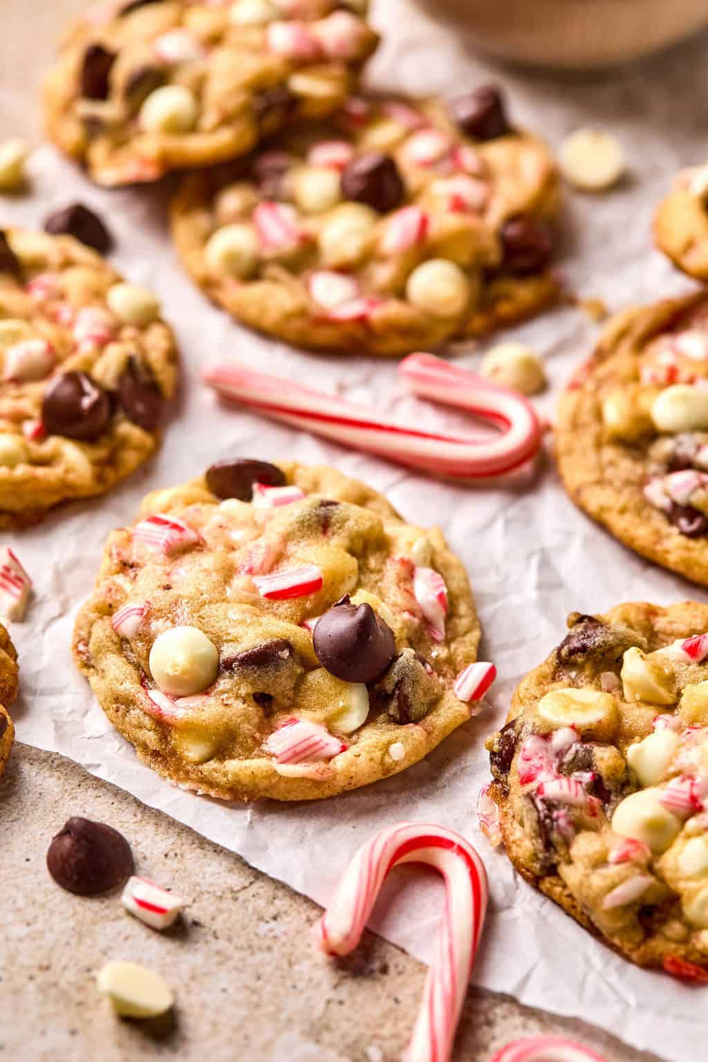 Chocolate and white chocolate peppermint cookies arranged on parchment paper with chips and candy canes surrounding.