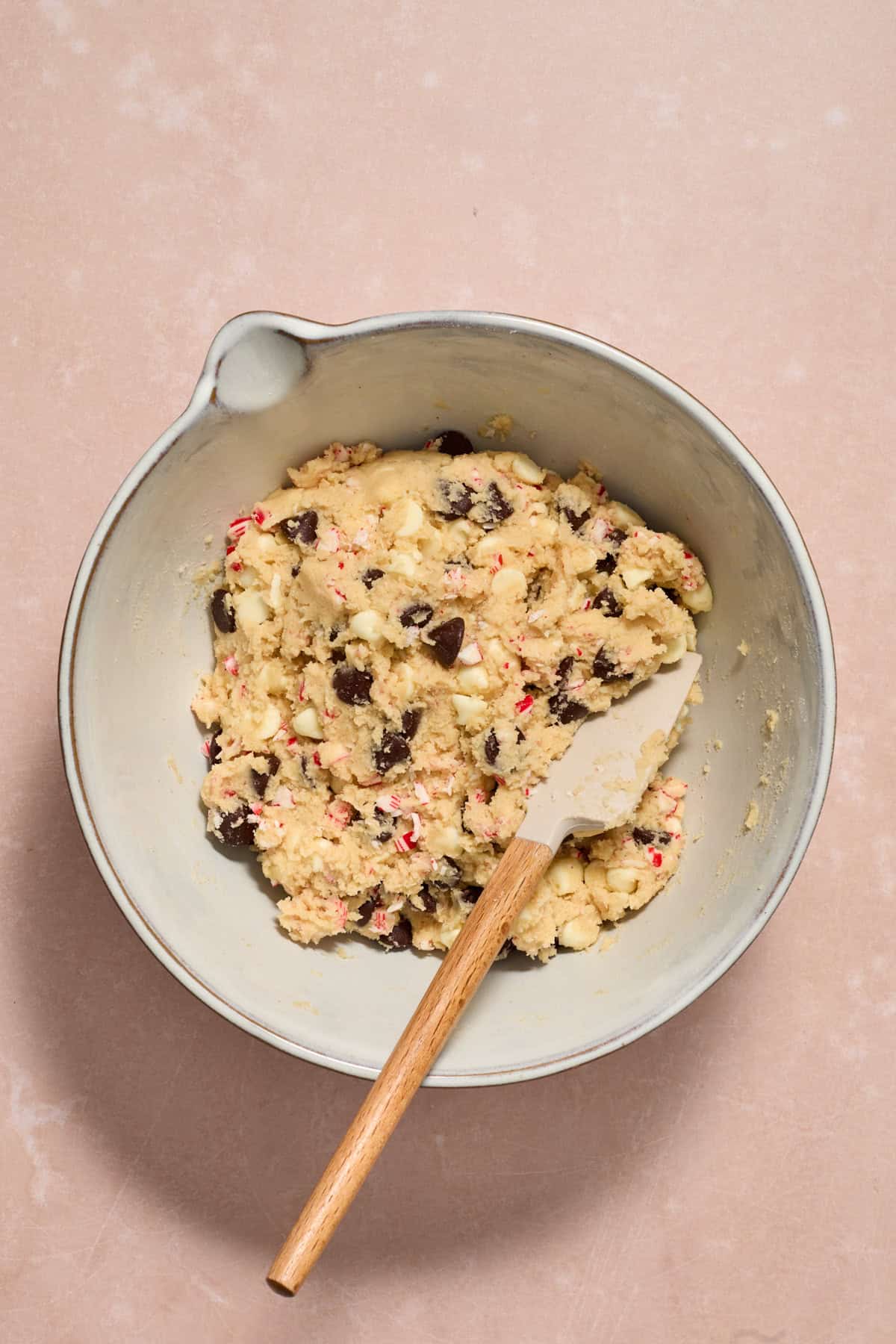 Prepared chocolate chip peppermint cookie dough in bowl with spatula.