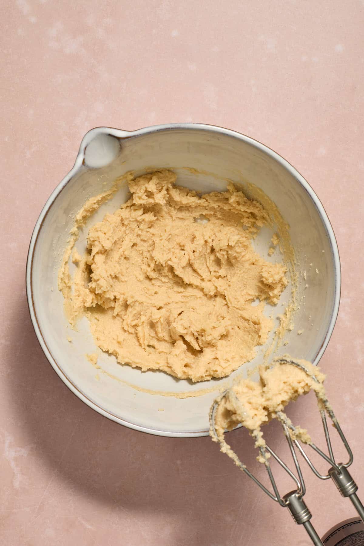 Creamed butter and sugar in mixing bowl with hand mixer propped next to it.