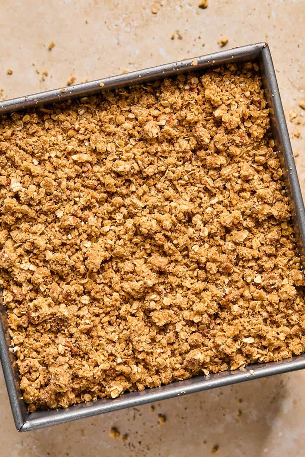 Pumpkin crisp in pan with oat topping covering pumpkin layer before baking.