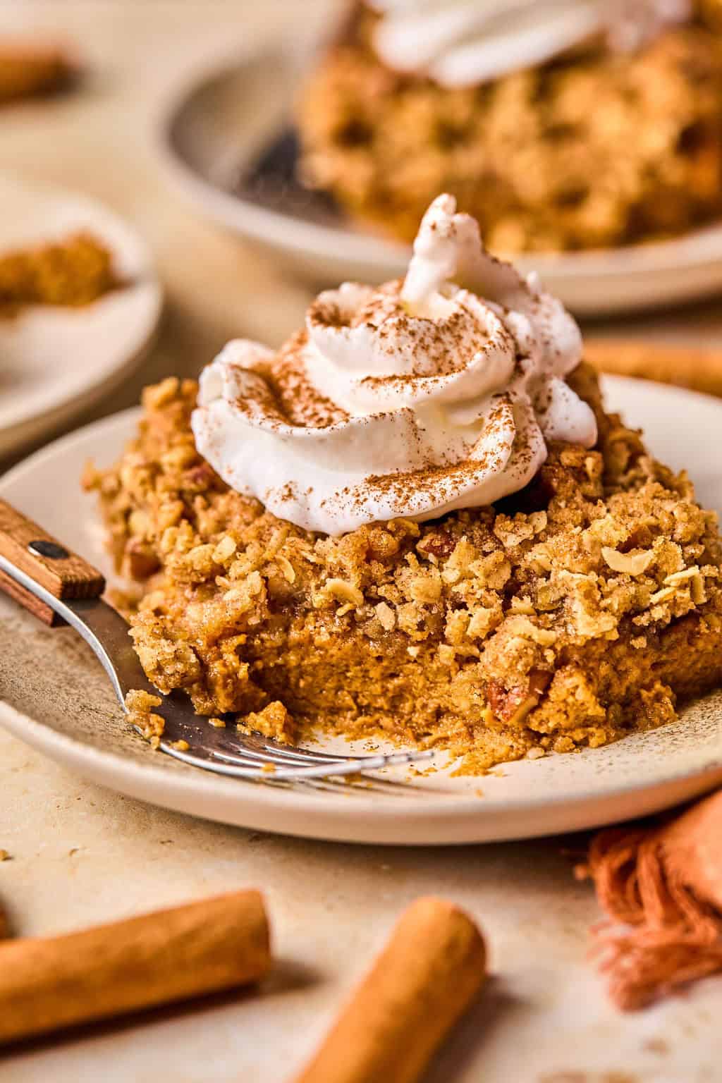 Pumpkin pie crumble slice on plate with whipped cream on top and fork propped beside it.