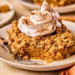 Slice of pumpkin pie crumble on plate with whipped cream and cinnamon over top and a fork on the plate beside it.
