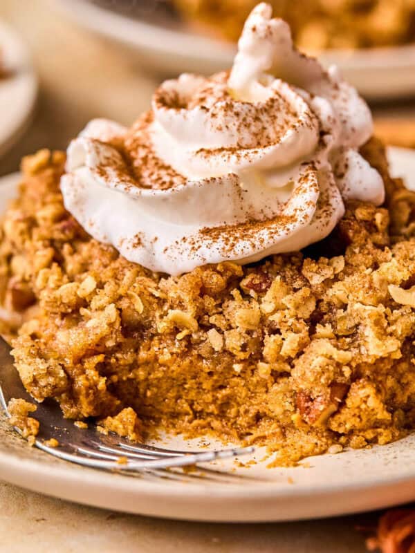 Slice of pumpkin pie crumble on plate with whipped cream and cinnamon over top and a fork on the plate beside it.