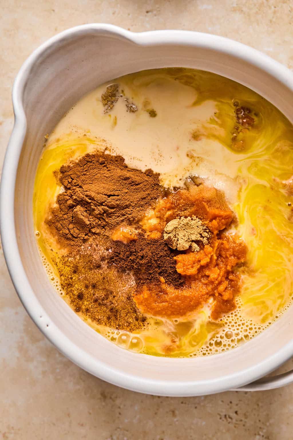 Pumpkin, butter, evaporated milk, sugar, and other ingredients in bowl before mixing.